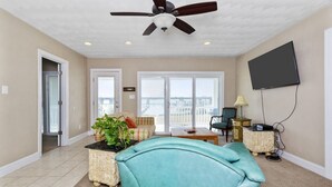 A spacious living room with a ceiling fan, a large window, a flat-screen TV, and a view of the outdoors.