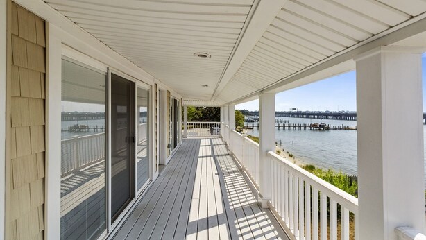 A covered wooden deck with a view of a water body and a pier in the distance.
