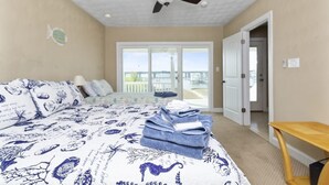 A bedroom with a bed, a ceiling fan, a view through a sliding glass door, and a wooden table.