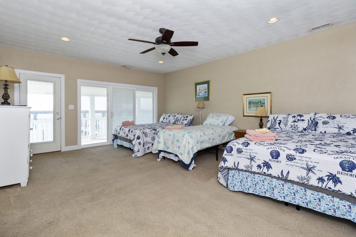 A bedroom with two beds, a ceiling fan, and a view of the outdoors through a sliding door.