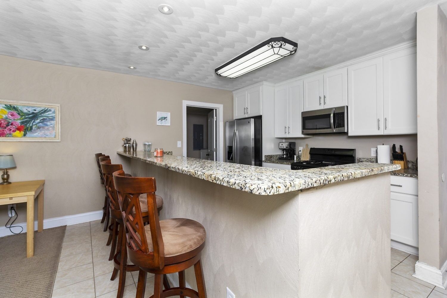 A kitchen with white cabinets, a granite countertop, a stainless steel refrigerator, and a microwave.