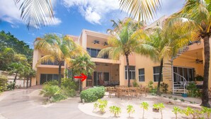 A hotel with a modern design, featuring a central courtyard with palm trees and outdoor seating. - Coral Sands #6 2 Bedroom Condo by RedAwning (Roatan)
