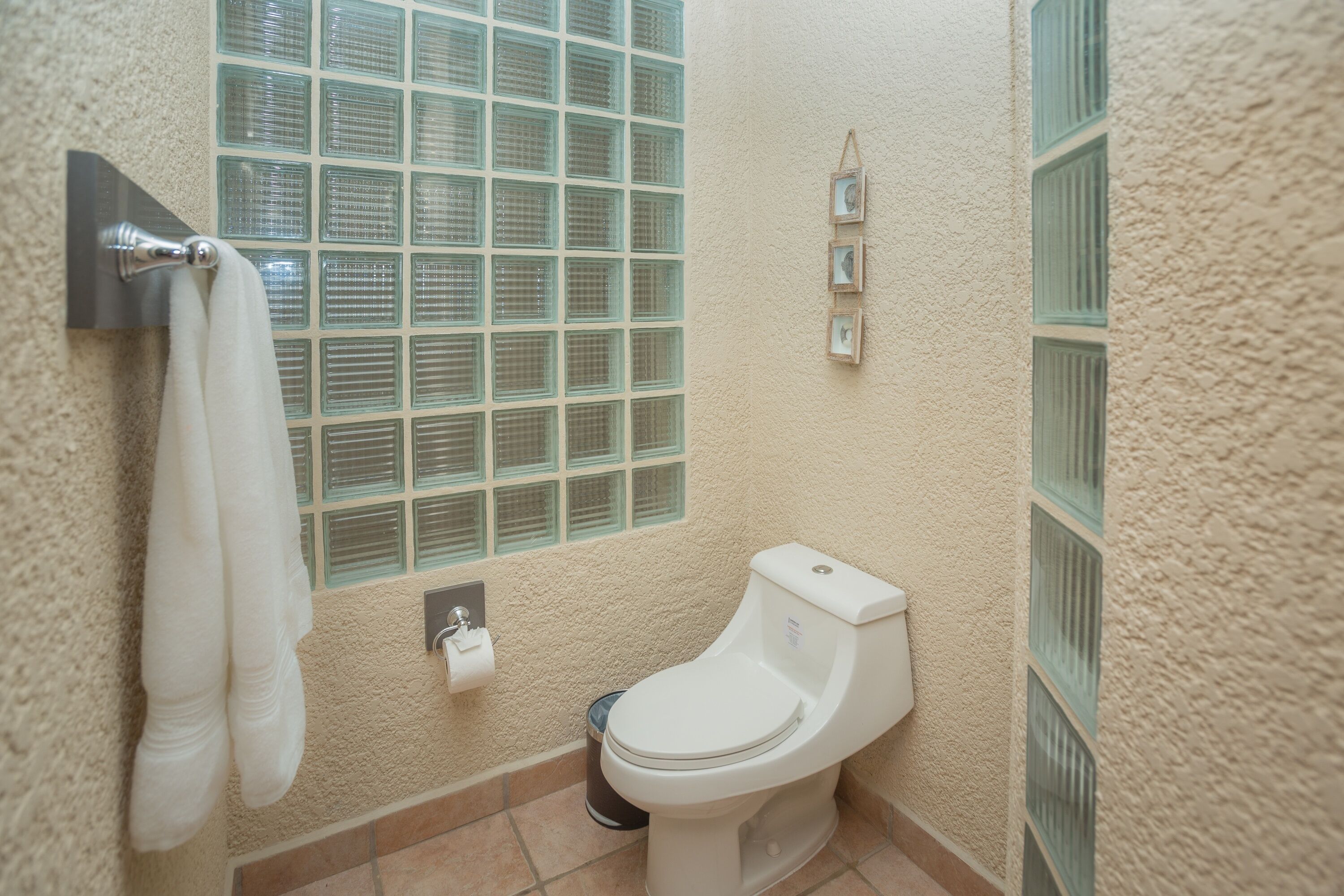 Un bagno con il water, un portasciugamani con due asciugamani, una finestra con un motivo a griglia e un cestino.