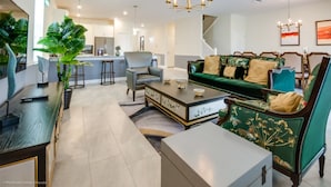 A spacious living area with a green sofa, a coffee table, and a dining area with a long table and chairs. - Villa in Champions Gate Resort 2527 (Davenport)