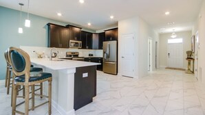 A modern kitchen with dark cabinets, stainless steel appliances, and a marble floor. - Villa in Champions Gate Resort 2523 (Davenport)
