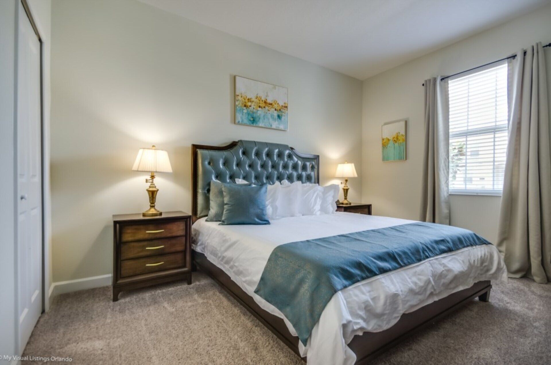 Une chambre à coucher avec un grand lit, deux tables de chevet avec des lampes, une tête de lit et des œuvres d’art accrochées aux murs.