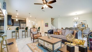 A spacious living room with a sofa, coffee table, and chairs. There is a kitchen area with a refrigerator and a dining table. - Villa in Champions Gate Resort 2523 (Davenport)
