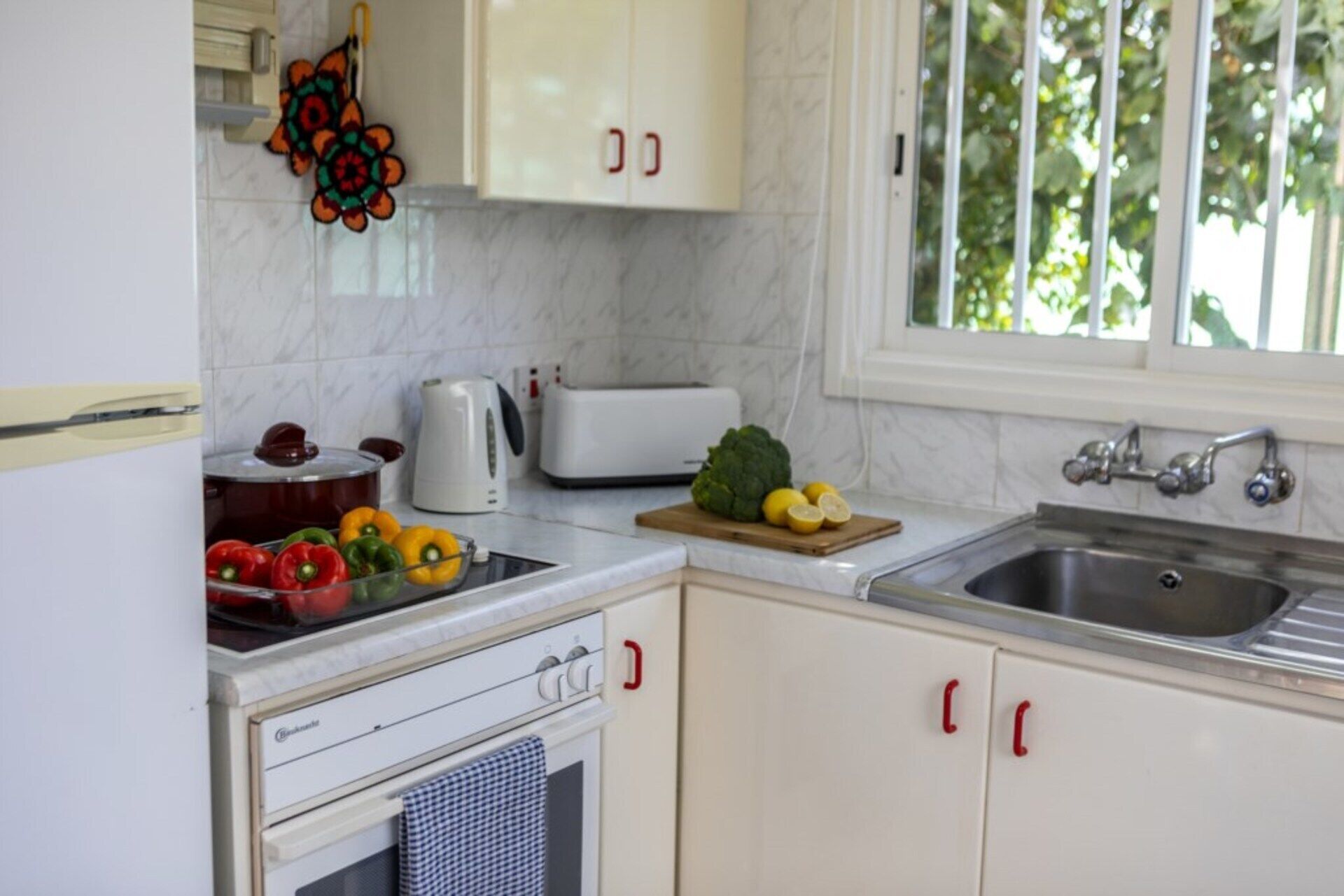 A kitchen with white cabinets, a sink, a stove, and a window with greenery outside.