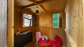 Een houten kamer met een bank, een tafel met stoelen en een raam met uitzicht op een boom.
