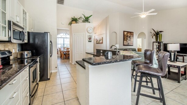 A spacious kitchen with a central island, dark countertops, and modern appliances. There is a dining area with a chandelier and a view of the outdoors. - Beautiful Villa With Private Pool, Orlando Villa 1488 (Davenport)