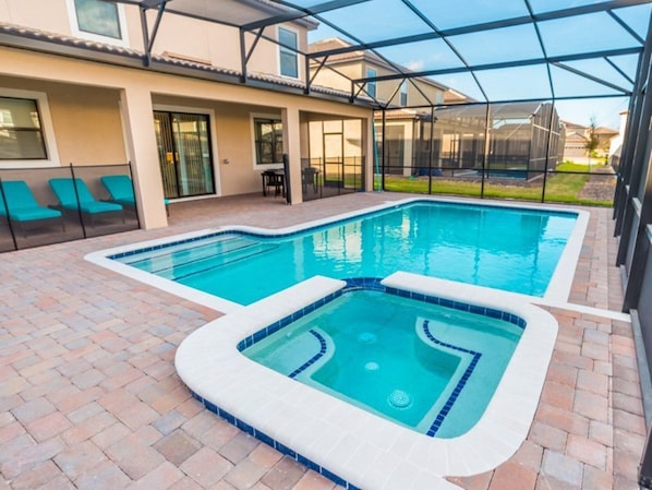 A swimming pool with a hot tub, surrounded by a covered patio area with chairs and a table.