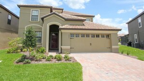 A two-story residential house with a tiled roof, a front entrance with a door, and a garage. - Villa in Champions Gate Resort 1010 (Davenport)