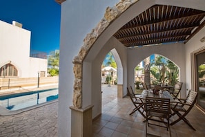 A covered outdoor area with a pool, stone pillars, and a table with chairs. - Private Villa in Pernera 1233 (Paralimni)