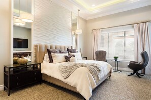 A modern hotel room with a large bed, a TV, a desk, and a chair.