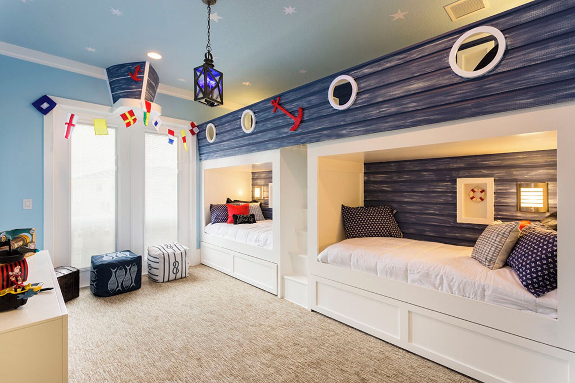 A room with bunk beds, a ceiling with nautical decorations, and a starry wall design.