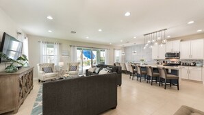 A spacious living room with a large sofa, a dining area with bar stools, and a kitchen with white cabinets and modern appliances. - Villa in Encore Resort at Reunion 3009 (Kissimmee)