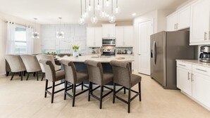 A modern kitchen with a central island, white cabinetry, stainless steel appliances, and a dining area with chairs. - Villa in Encore Resort at Reunion 3009 (Kissimmee)
