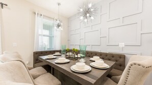 A dining area with a dark wood table, white plates, and green glassware. There are two pendant lights above the table. - Villa in Encore Resort at Reunion 3009 (Kissimmee)