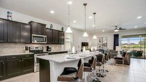 A modern kitchen with dark cabinets, a large island with bar stools, a microwave, and a coffee maker. - Villa in Windsor at Westside Resort 3090 (Kissimmee)