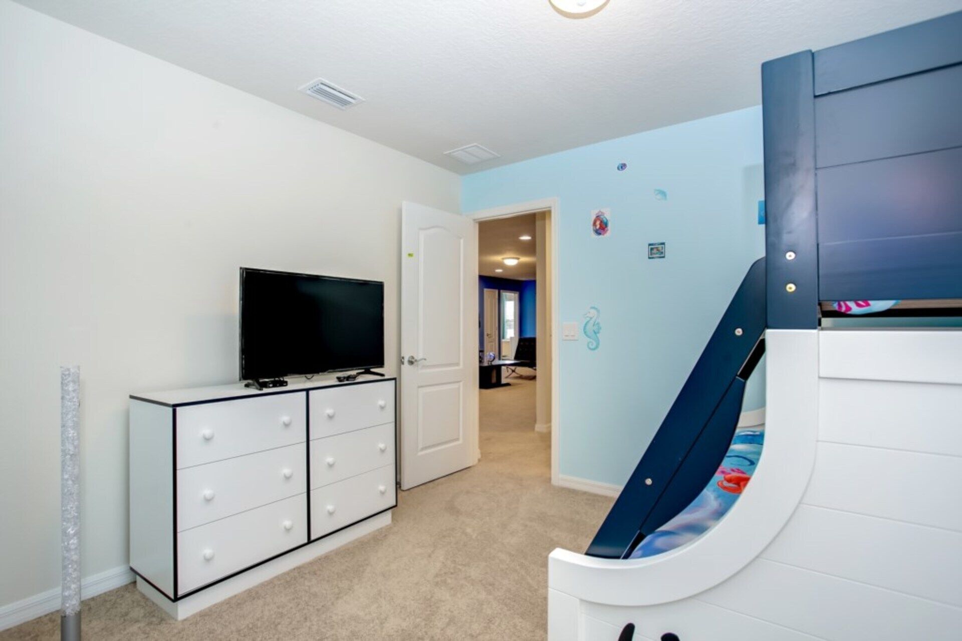 A room with a television on a white cabinet, a door leading to another room, and a blue wall with a seahorse decoration.