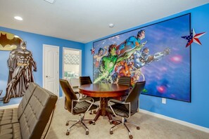 A conference room with a round table, four chairs, and a large wall mural featuring superheroes. - Villa in Windsor at Westside Resort 3090 (Kissimmee)
