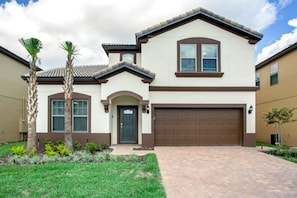 A two-story house with a brown garage door, a front entrance with a door, and a small porch area. - Villa in Windsor at Westside Resort 3090 (Kissimmee)