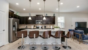 A modern kitchen with dark cabinets, stainless steel appliances, and a central island with bar stools. - Villa in Windsor at Westside Resort 3090 (Kissimmee)