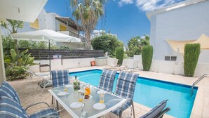 A poolside area with a glass table set for dining, lounge chairs, and a swimming pool.