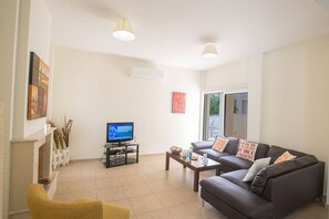 A living room with a sofa, a yellow armchair, a coffee table, a TV, and a fireplace.