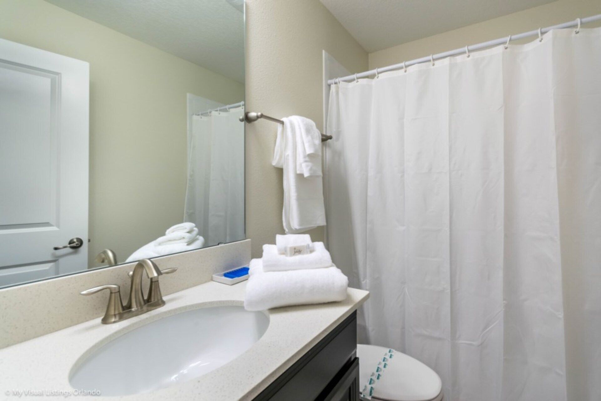 A bathroom with a white sink, a mirror, a towel rack, and a shower curtain.