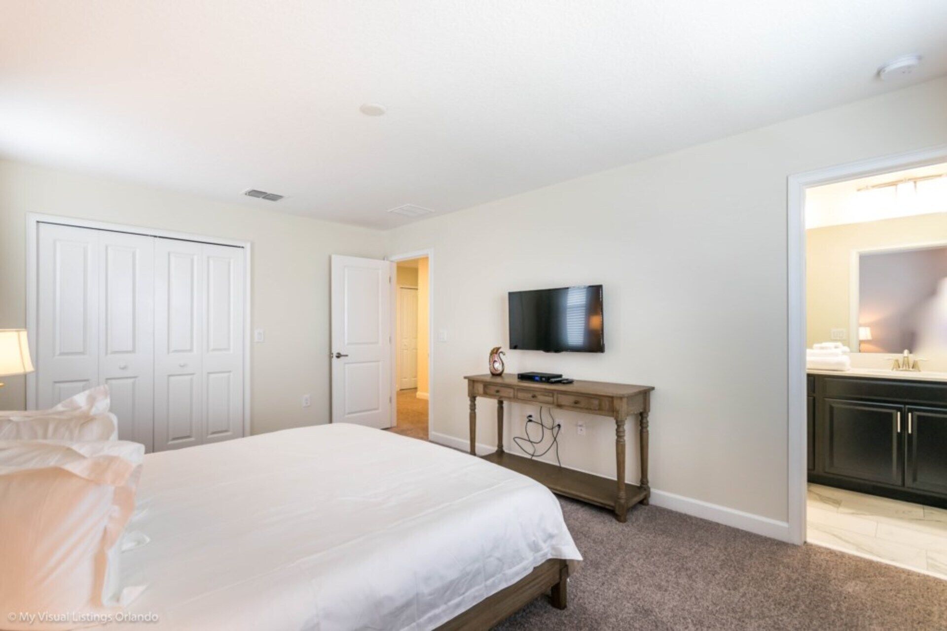A bedroom with a bed, a TV on a wooden stand, and a door leading to a bathroom.