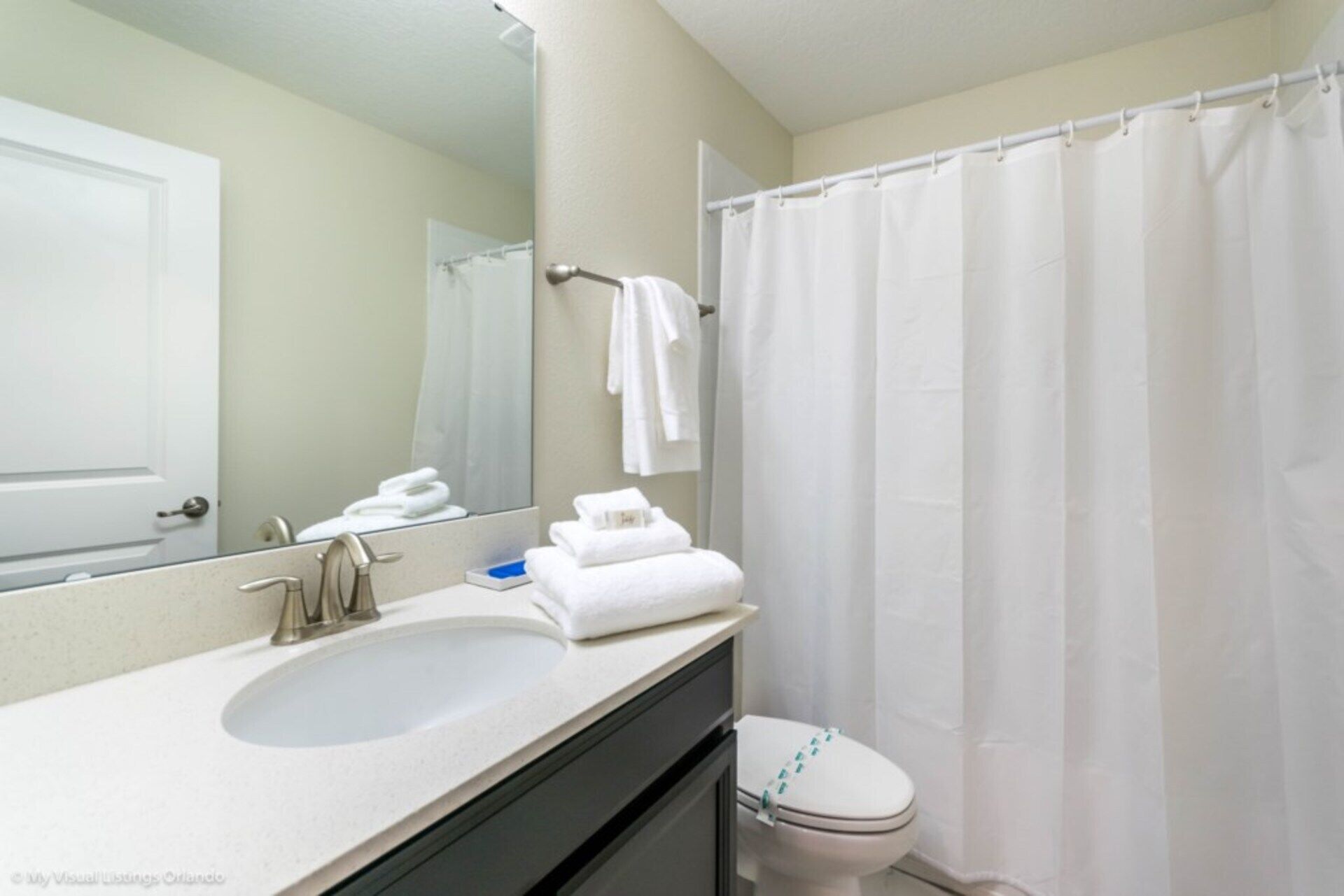 Une salle de bain avec un lavabo blanc, un miroir, un porte-serviettes avec des serviettes et un rideau de douche.