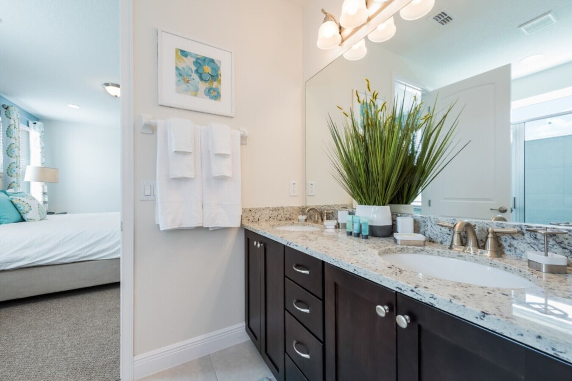 A modern bathroom with a large mirror, a sink with a marble countertop, and a potted plant.