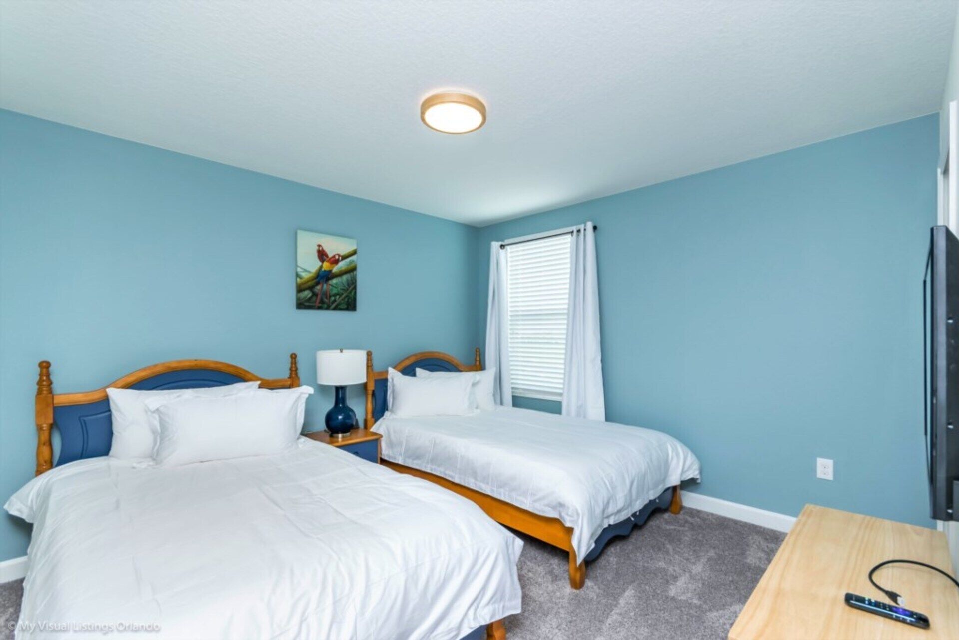 A bedroom with two beds, a nightstand with a lamp, a painting on the wall, and a window with blinds.