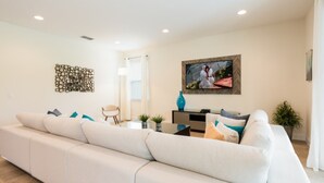 Una sala de estar moderna con un sofá blanco grande, un televisor de pantalla plana montado en la pared y un elemento decorativo en la pared.