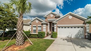 A two-story residential building with a garage, a well-maintained lawn, and a palm tree. - Villa in Windsor Palms Resort 1217 (Kissimmee)