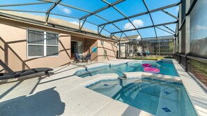 A swimming pool with a glass enclosure, lounge chairs, and a covered patio area. - Villa in Windsor Palms Resort 1217 (Kissimmee)