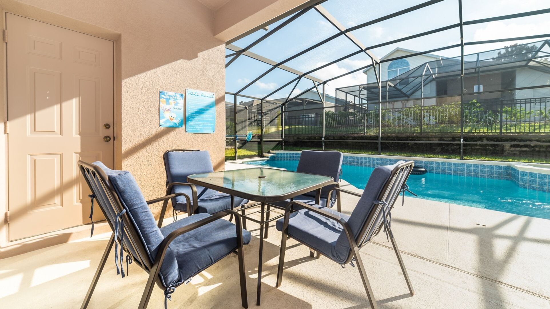 A glass-enclosed pool area with a table and chairs, a door, and two informational posters on the wall.