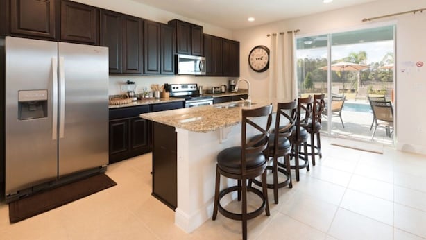 A modern kitchen with dark cabinets, stainless steel appliances, a granite countertop, and a bar area with stools. - Villa in Encore Resort at Reunion 1995 (Kissimmee)