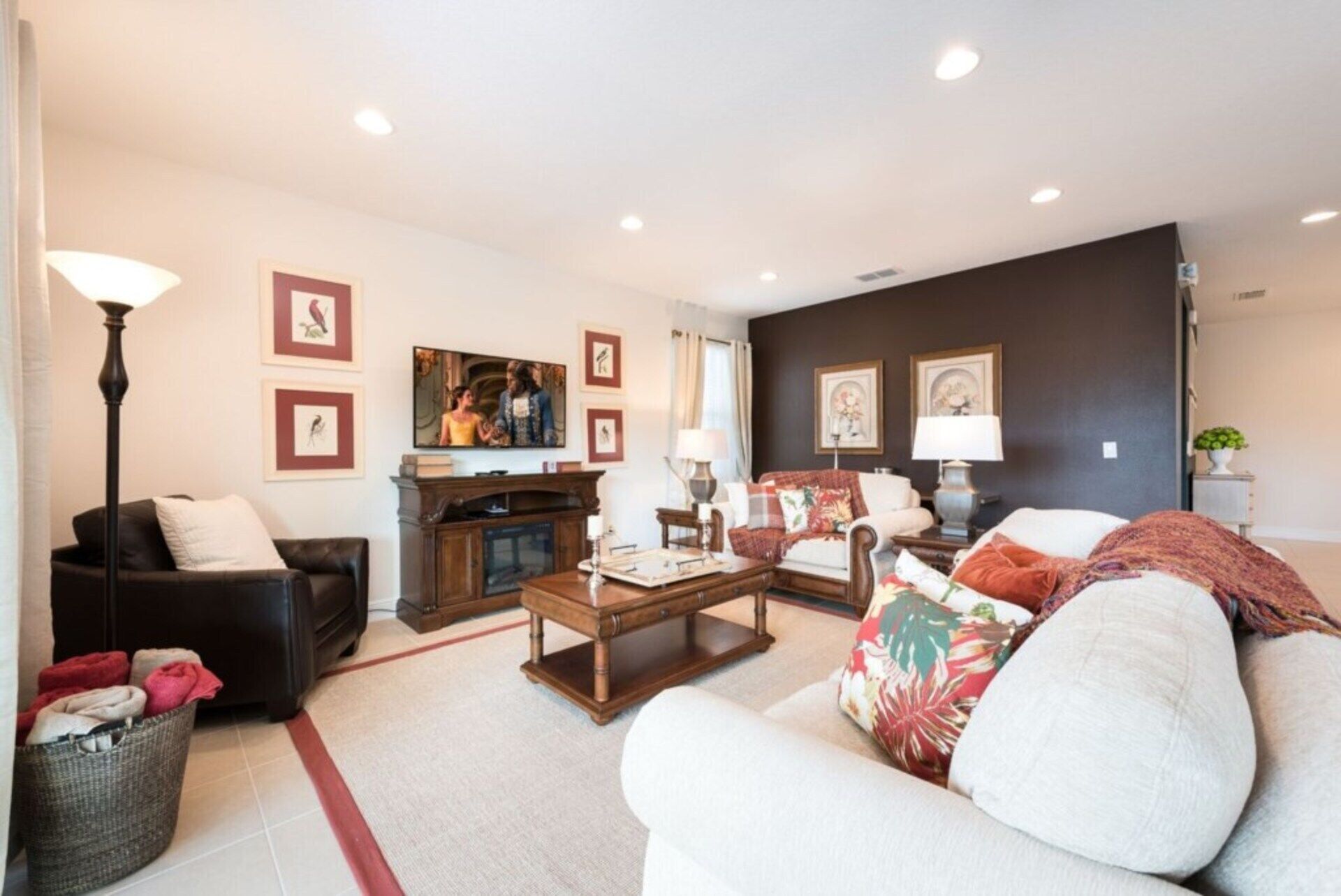 A living room with a sofa, armchair, coffee table, and a fireplace. There are framed pictures on the wall and a lamp on a side table.