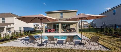 A backyard with a swimming pool, lounge chairs, and umbrellas.