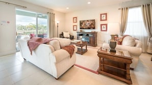 A living room with a sofa, armchairs, a coffee table, and a TV. There is a balcony with a view outside. - Villa in Encore Resort at Reunion 1995 (Kissimmee)