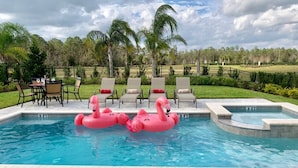 A swimming pool with two pink flamingo floats, a hot tub, and a patio area with chairs and a table. - Villa in Encore Resort at Reunion 1995 (Kissimmee)