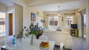 A spacious living area with a sofa, dining table with chairs, a TV stand, and a large window with curtains. - Beautiful Villa With Private Pool, Protaras Villa 1010 (Paralimni)