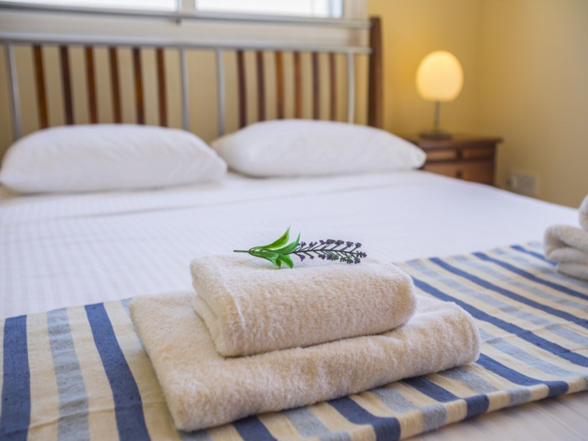 A neatly made bed with white pillows and a folded towel on a striped blanket.