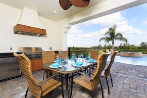 An outdoor dining area with wicker chairs and a glass table, overlooking a swimming pool and palm trees. - Villa in Reunion Resort & Spa 1313 (Kissimmee)