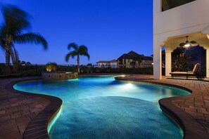 A swimming pool with a curved design, surrounded by brick walkways and palm trees. - Villa in Reunion Resort & Spa 1313 (Kissimmee)