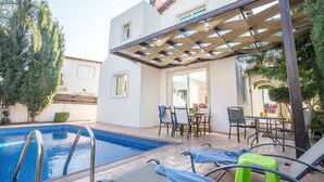 Et poolområde med pergola, liggestole og et spisebord.