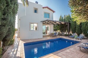 Una casa moderna de dos pisos con piscina, muebles de patio y una pérgola.