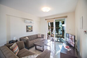 Un soggiorno moderno con divano, tavolino da caffè e televisore a schermo piatto. Una porta scorrevole in vetro dà accesso a un'area esterna con tavolo e sedie.